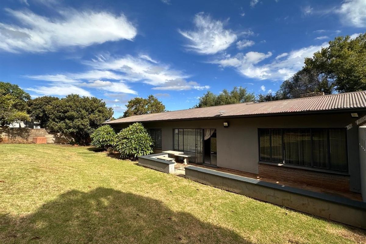Rear view of the property featuring a spacious lawn, a paved patio area with built-in seating, and a corrugated metal roof.