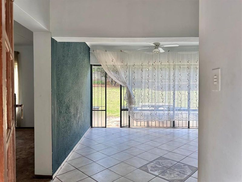 A bright living area featuring tiled flooring, a ceiling fan, and direct access to the rear garden through a security gate.