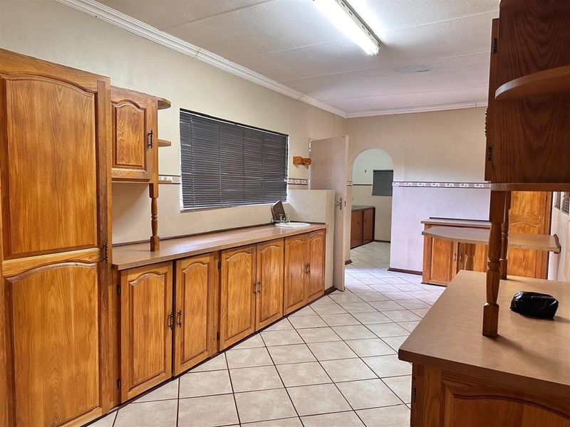 A functional kitchen featuring extensive wooden cabinetry, tiled flooring, and a neutral color palette, offering a practical layout with potential for modernization.