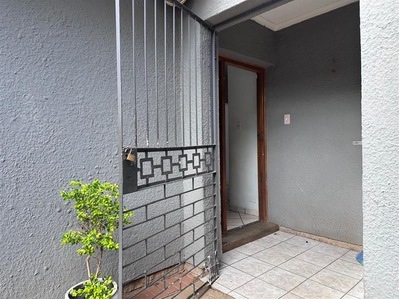 A functional exterior entrance area featuring a security gate, tiled flooring, and a textured grey wall finish.