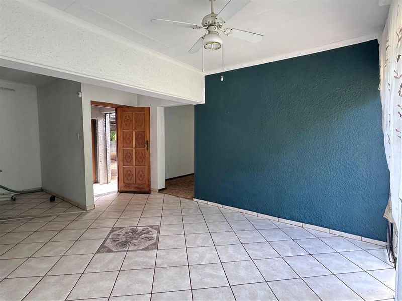 An open plan living area featuring tiled flooring, a ceiling fan, and a prominent dark blue accent wall leading to an exterior entrance.