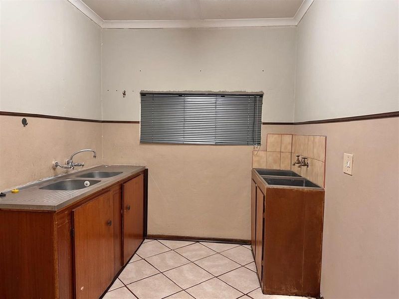 A functional laundry or utility room featuring dual stainless steel sink units, wooden cabinetry, and tiled flooring.