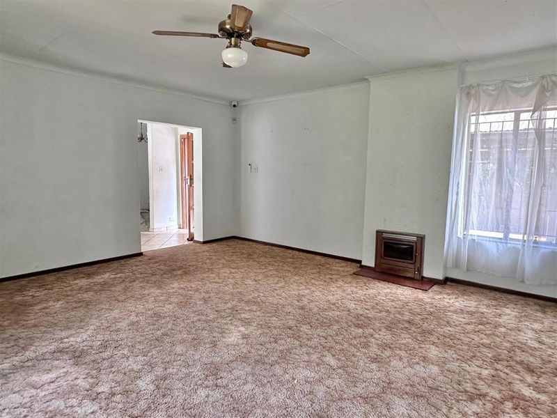 Spacious living room featuring a built-in fireplace, ceiling fan, and carpeted flooring, offering a blank canvas for renovation.