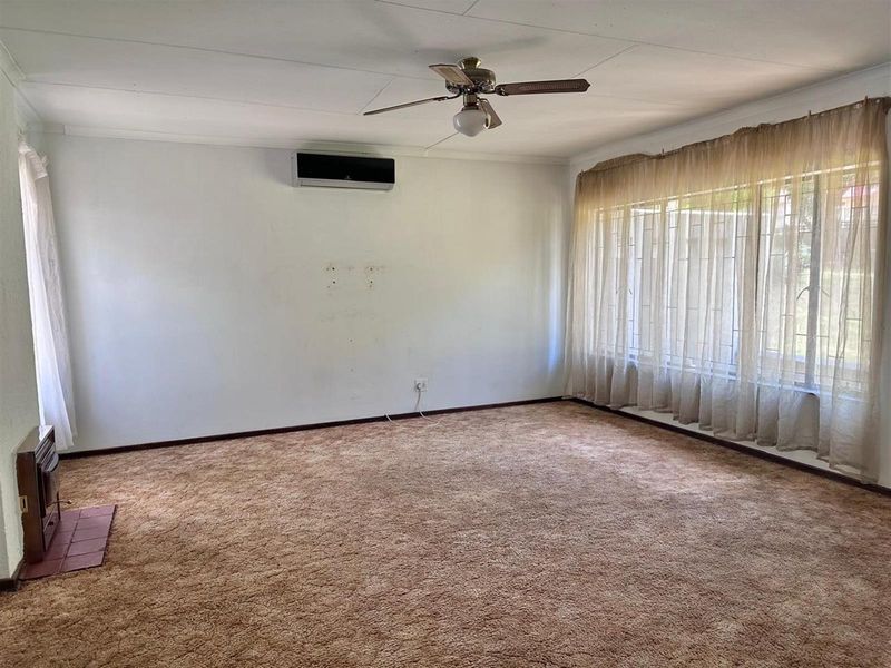 Spacious living room featuring wall-mounted air conditioning, a ceiling fan, and large windows with natural light, finished with carpeted flooring.