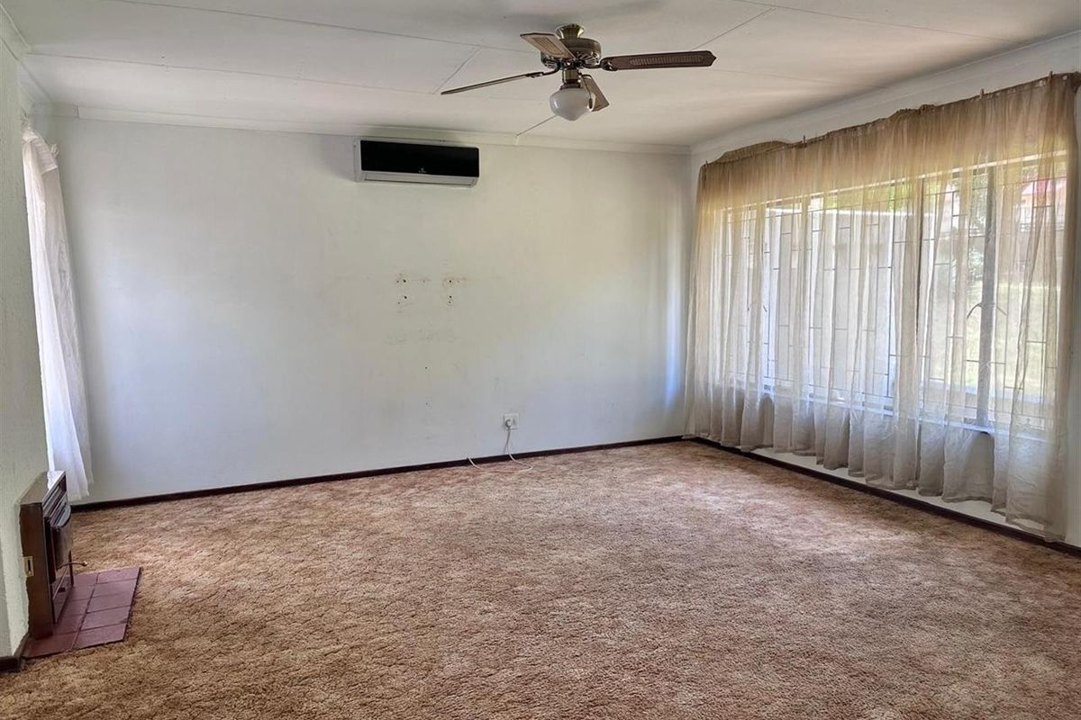Spacious living room featuring wall-mounted air conditioning, a ceiling fan, and large windows with natural light, finished with carpeted flooring.