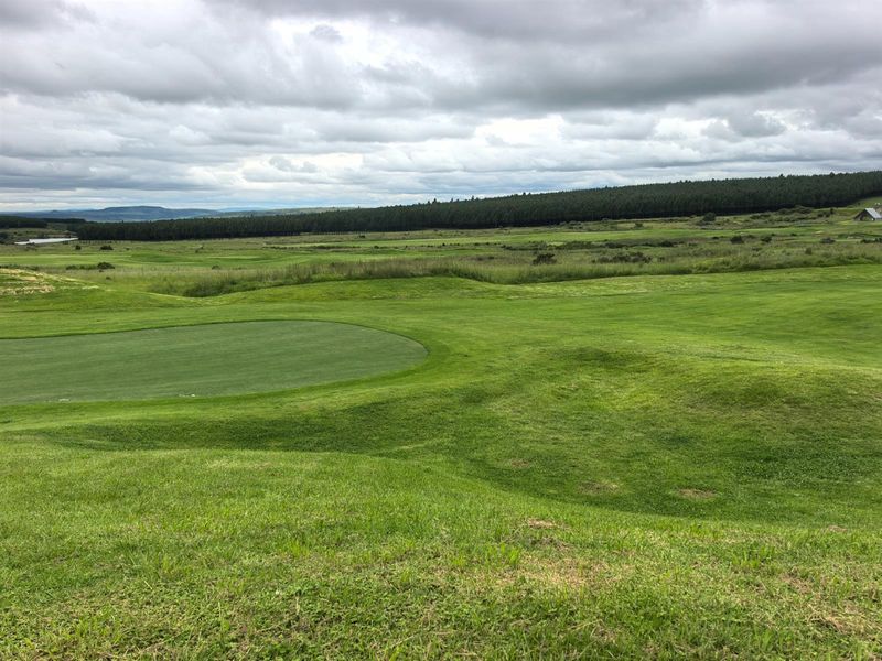 A scenic view overlooking a well-maintained golf course and expansive green landscape under a cloudy sky.