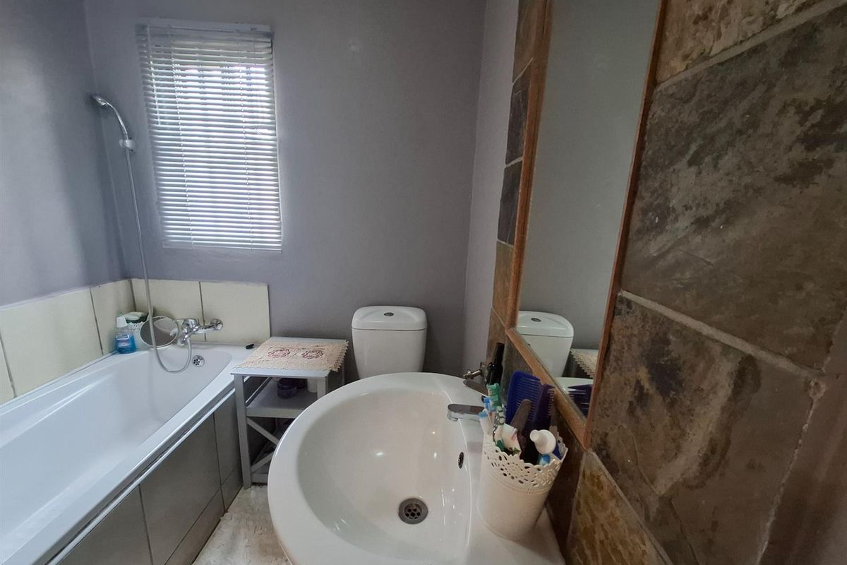 A functional bathroom featuring a built-in bathtub with shower attachment, a pedestal basin, and a wall-mounted mirror with stone-look tile surround.