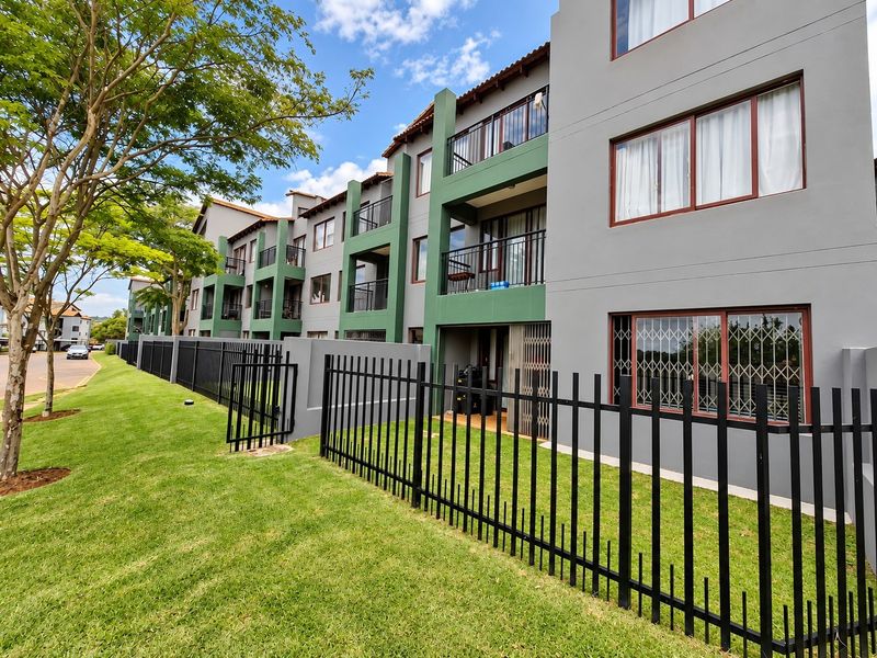 Exterior view of a modern apartment complex featuring multi-level balconies, secure metal fencing, and well-maintained green lawn areas.