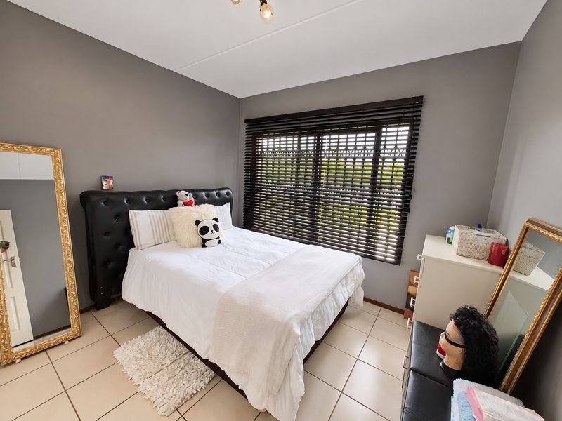 A well-maintained bedroom featuring neutral grey walls, tiled flooring, and dark venetian blinds, providing a clean and functional living space.