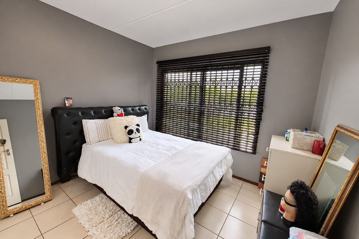 A well-maintained bedroom featuring neutral grey walls, tiled flooring, and dark venetian blinds, providing a clean and functional living space.