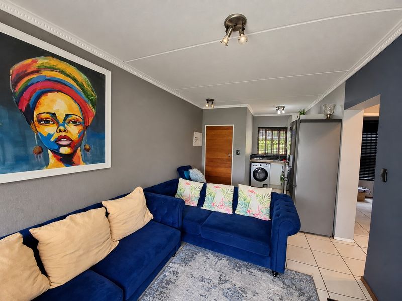 Open-plan living area featuring tiled flooring, decorative ceiling cornices, and a compact kitchen and laundry utility space.