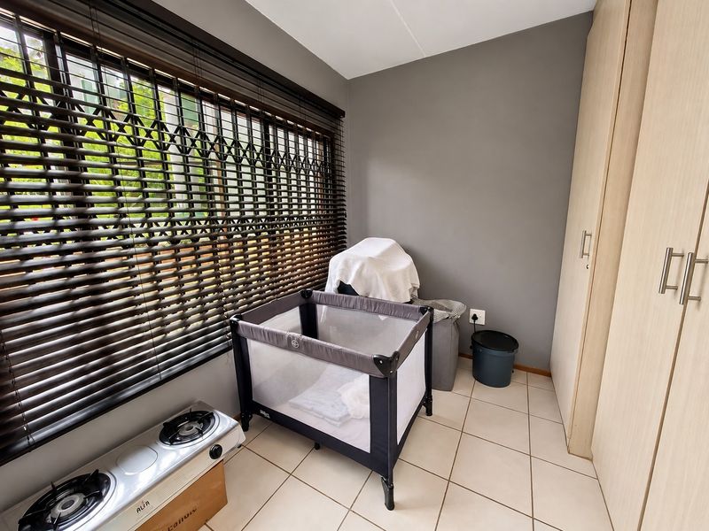A bedroom featuring tiled flooring, built-in cupboards, and a security gate over the window.