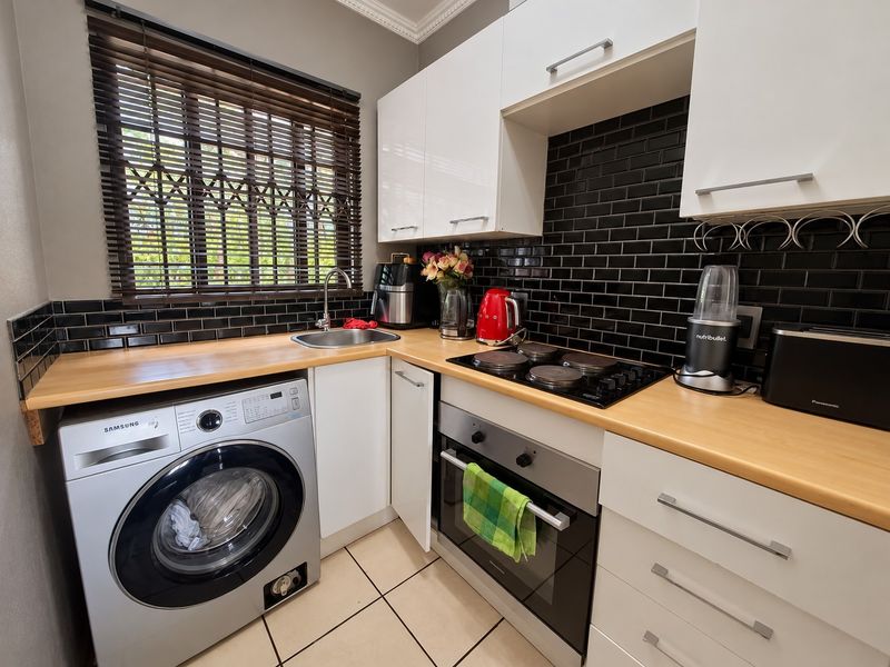 A compact, well-maintained kitchen featuring white cabinetry, black subway tile backsplash, wood-look countertops, and integrated appliances including an oven and hob.
