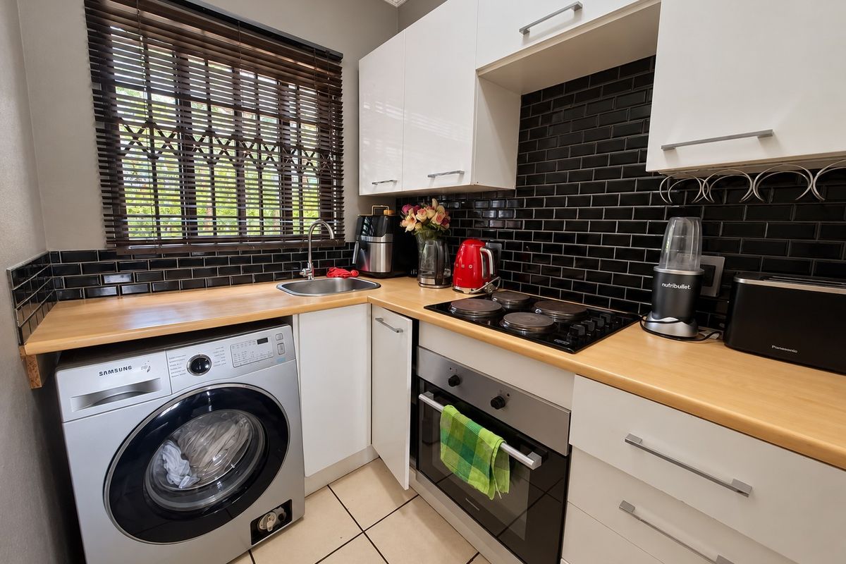 A compact, well-maintained kitchen featuring white cabinetry, black subway tile backsplash, wood-look countertops, and integrated appliances including an oven and hob.