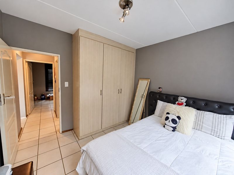 A well-maintained bedroom featuring neutral grey walls, light wood-finish built-in wardrobes, and tiled flooring, leading into a hallway.