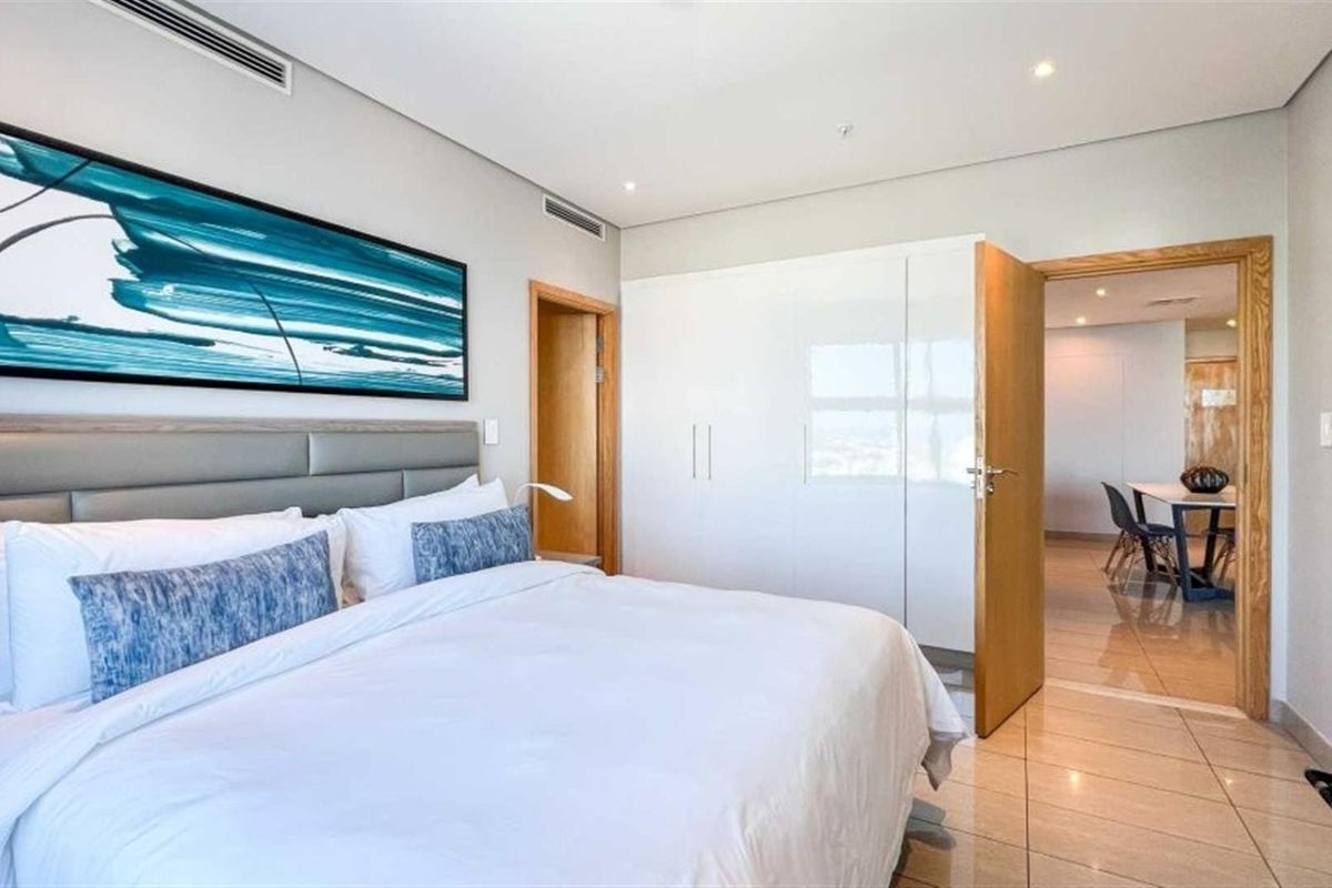 A well-maintained bedroom featuring built-in high-gloss wardrobes, recessed ceiling lighting, and tiled flooring, with direct access to an adjacent living area.