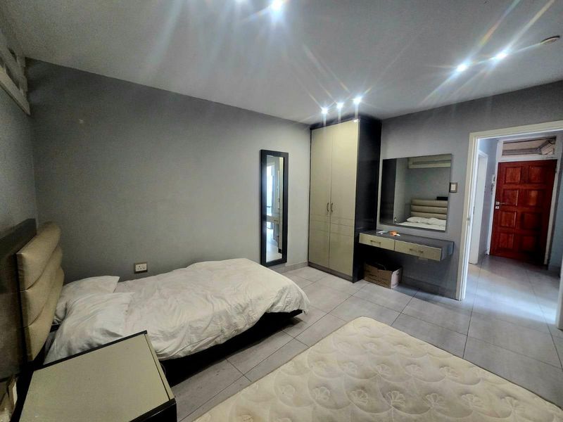 A bedroom featuring tiled flooring, recessed downlights, a built-in wardrobe, and a wall-mounted vanity unit with a mirror.