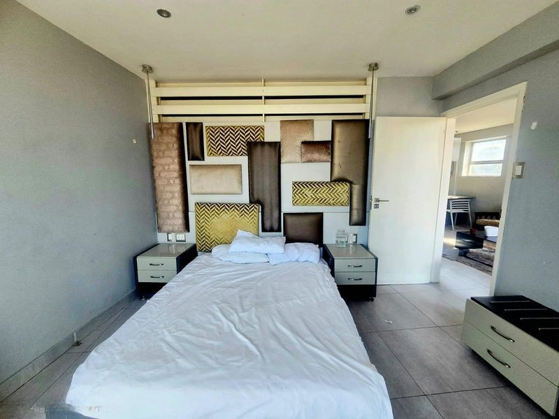 A bedroom featuring tiled flooring, recessed downlighting, and a decorative headboard wall panel, with an adjacent room visible through the doorway.