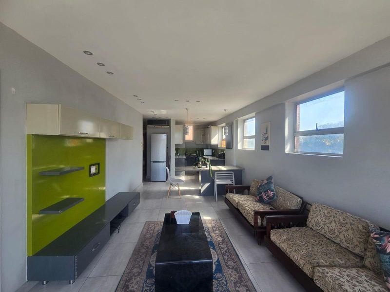 Open-plan living and kitchen area featuring tiled floors, recessed lighting, and a functional kitchen layout with granite countertops and built-in cabinetry.