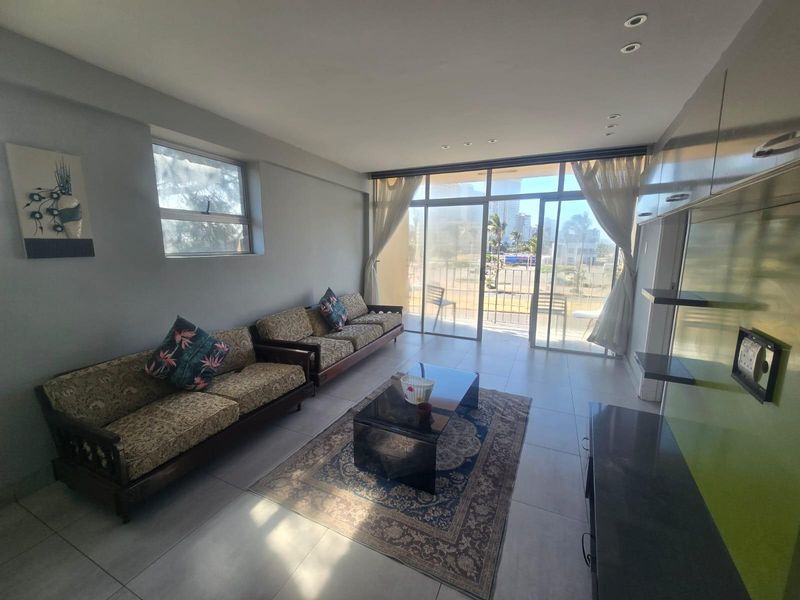 A bright living room featuring large sliding glass doors leading to a balcony, tiled flooring, and built-in wall cabinetry with recessed lighting.