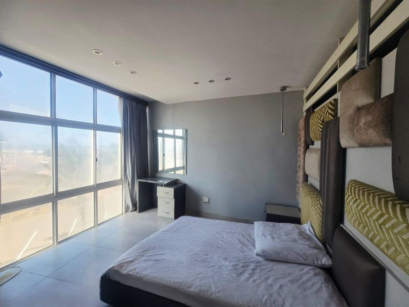 A bright bedroom featuring large floor-to-ceiling windows, tiled flooring, recessed lighting, and a built-in vanity area.