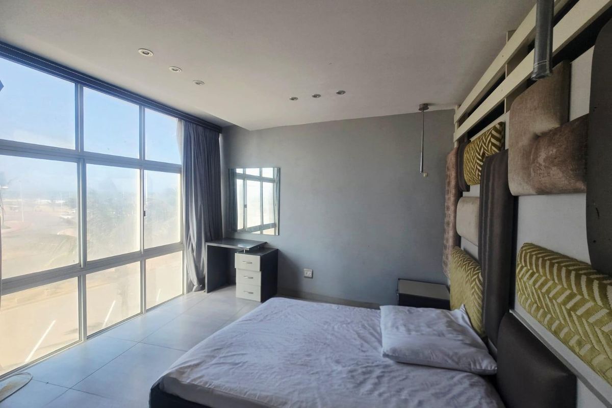 A bright bedroom featuring large floor-to-ceiling windows, tiled flooring, recessed lighting, and a built-in vanity area.