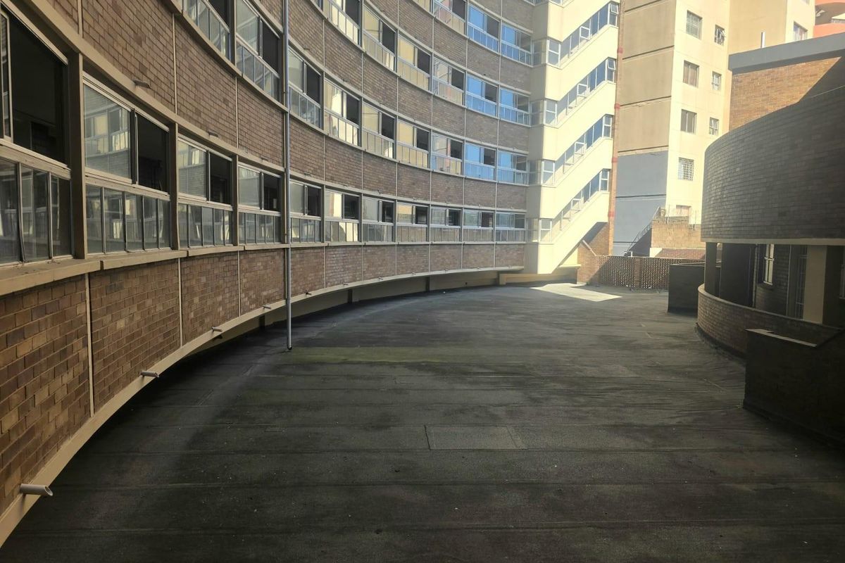 A view of a curved brick apartment building exterior featuring a large concrete terrace area and external stairwell access.