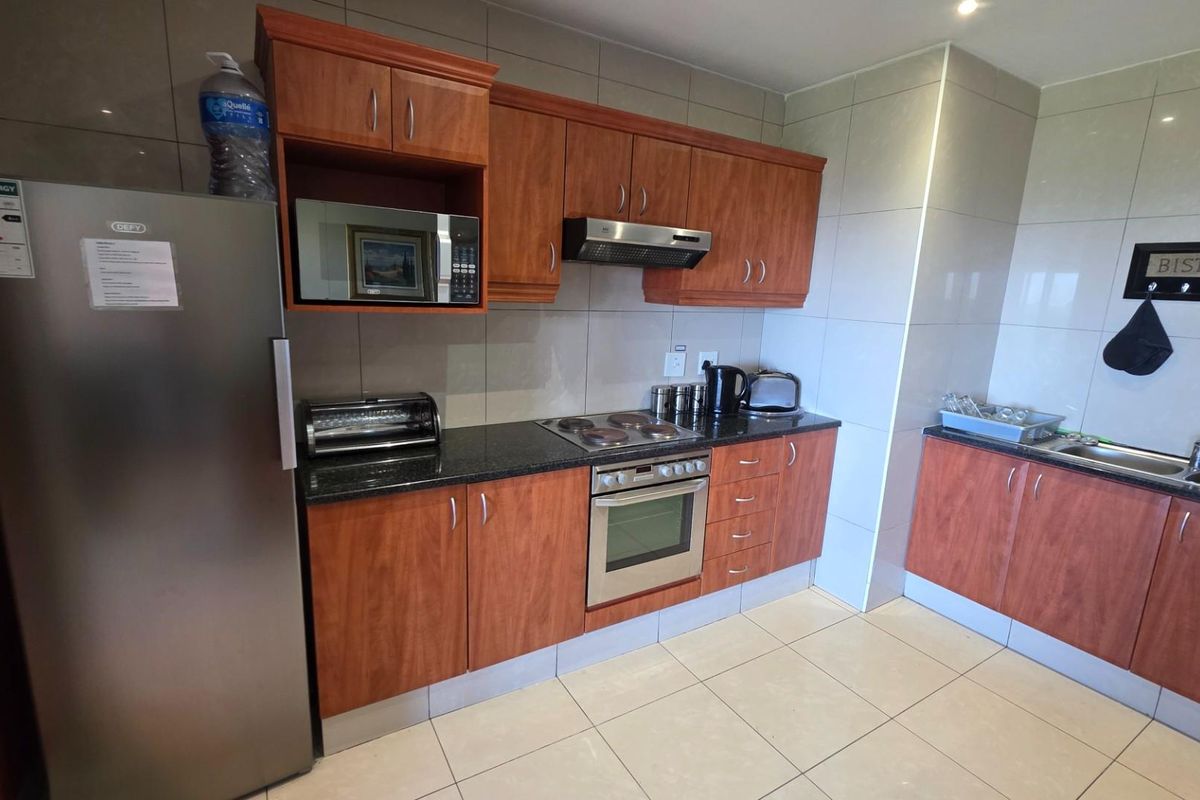 A functional kitchen featuring wood-finish cabinetry, granite countertops, a built-in oven, hob, and extractor fan, complemented by tiled flooring and wall splashbacks.