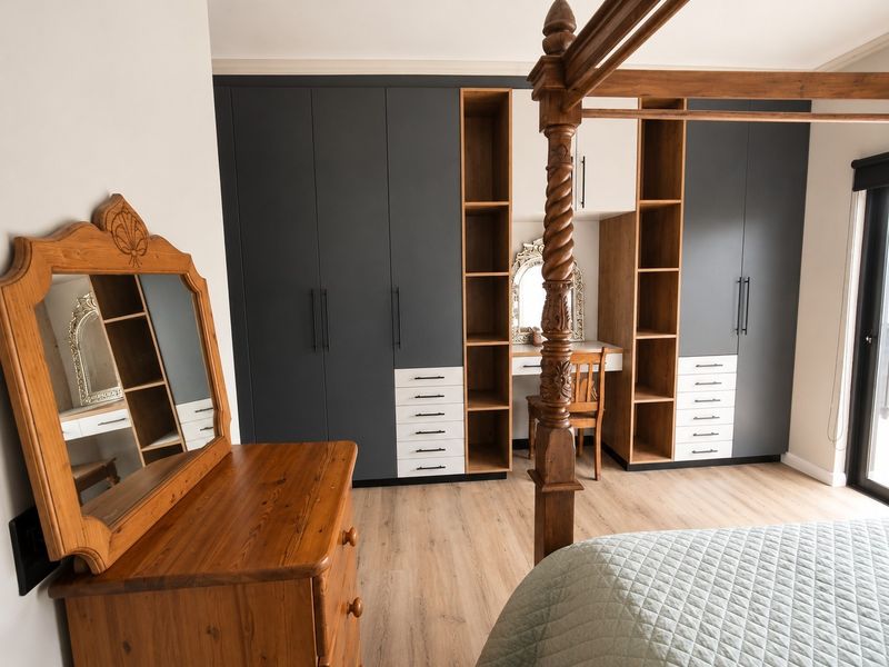 A well-appointed bedroom featuring modern built-in cupboards with integrated vanity shelving, laminate flooring, and a sliding door providing natural light.