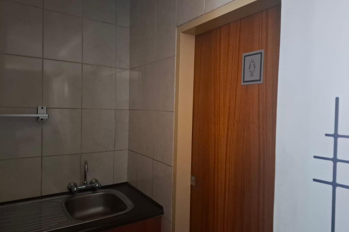 A functional industrial restroom area featuring a stainless steel sink basin, tiled splashback, and a wooden door with signage.