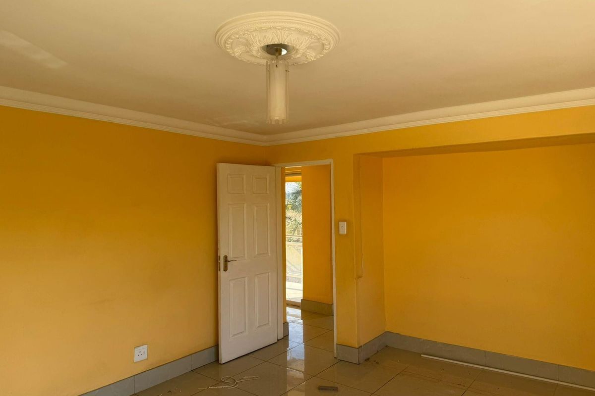 An empty interior room featuring yellow painted walls, tiled flooring, decorative ceiling rose, and a doorway leading to an adjacent space.