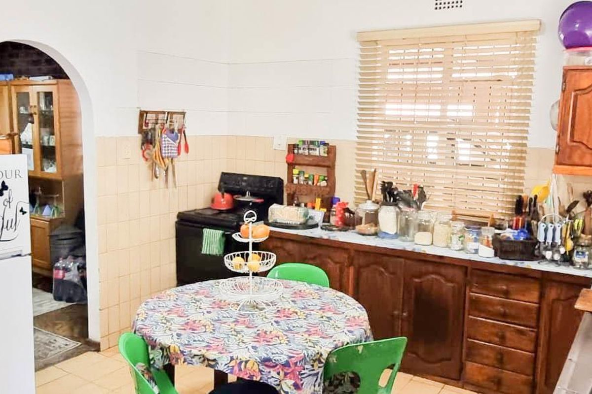 A dated kitchen featuring traditional wooden cabinetry, tiled splashbacks, and a functional layout with an arched doorway leading to an adjacent space.