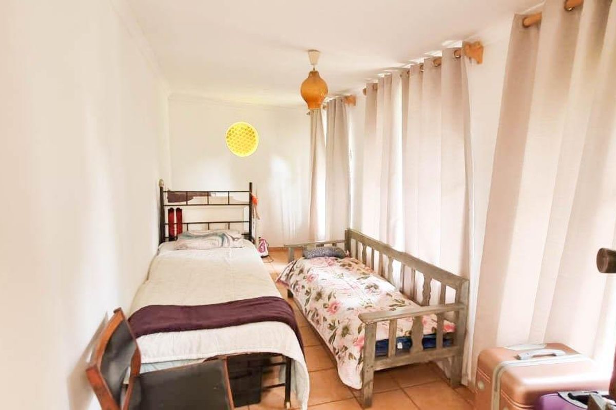 A functional bedroom featuring tiled flooring, large windows with curtains, and a simple pendant light fixture.