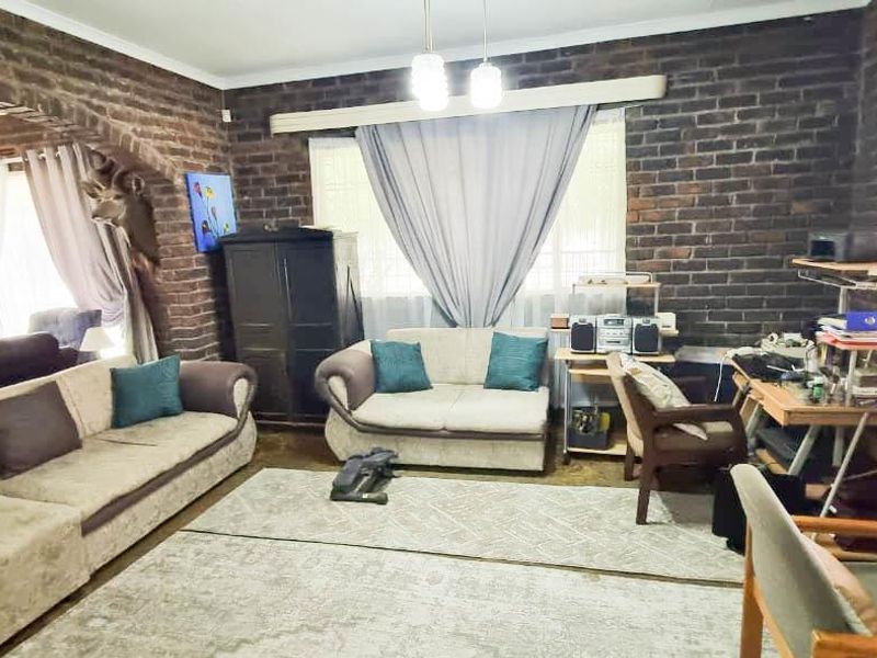 Spacious living room featuring rustic exposed brick walls, a distinctive brick archway, and natural light through large windows with venetian blinds.