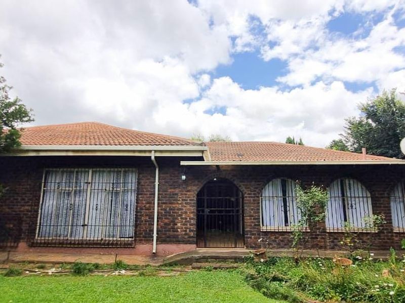Rear view of a face brick house featuring a tiled roof, arched entrance, and security bars on windows, set within a garden area.