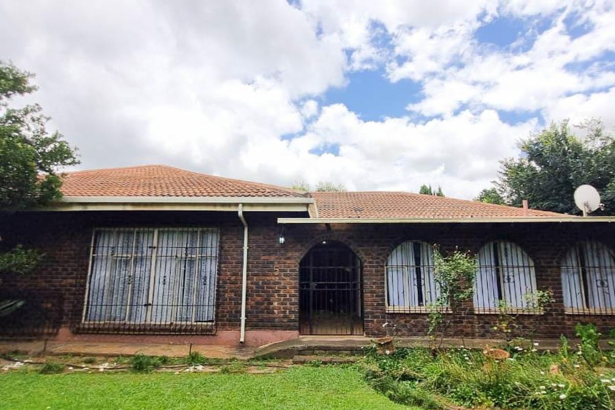 Rear view of a face brick house featuring a tiled roof, arched entrance, and security bars on windows, set within a garden area.