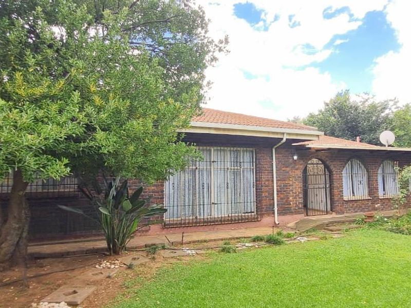 Rear view of a face brick house featuring arched windows, security gates, and a surrounding garden area.