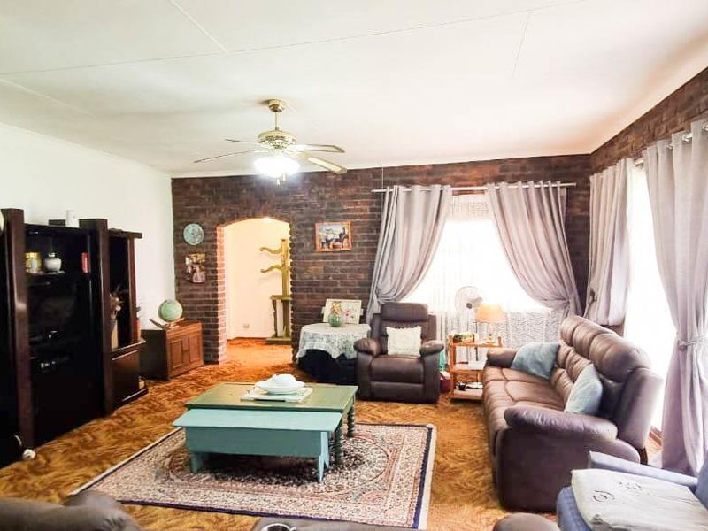 A spacious living room featuring an exposed brick accent wall, a ceiling fan, and an arched entryway leading to adjacent living areas.