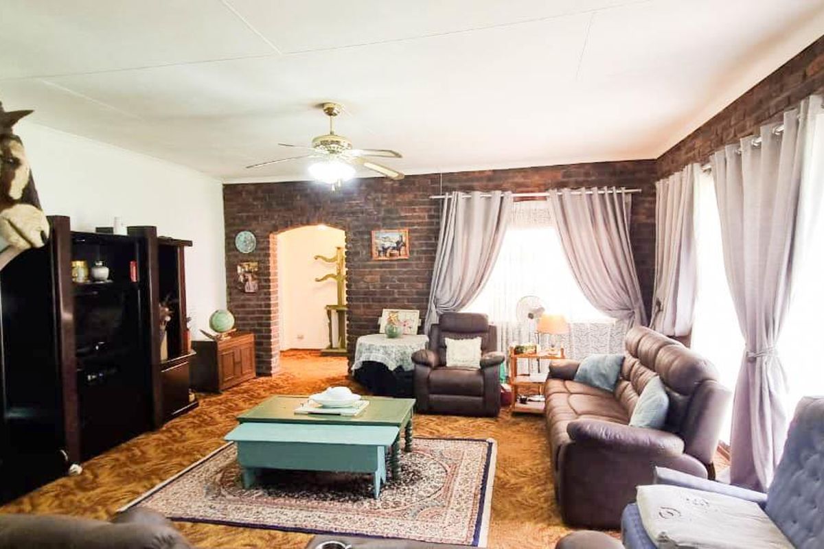 A spacious living room featuring an exposed brick accent wall, a ceiling fan, and an arched entryway leading to adjacent living areas.