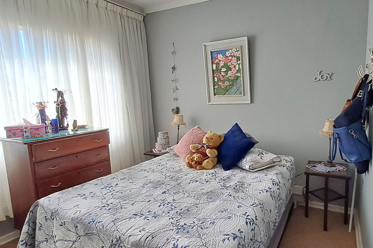 A cozy bedroom featuring neutral wall tones, carpeted flooring, and large windows with floor-to-ceiling curtains, providing ample natural light.