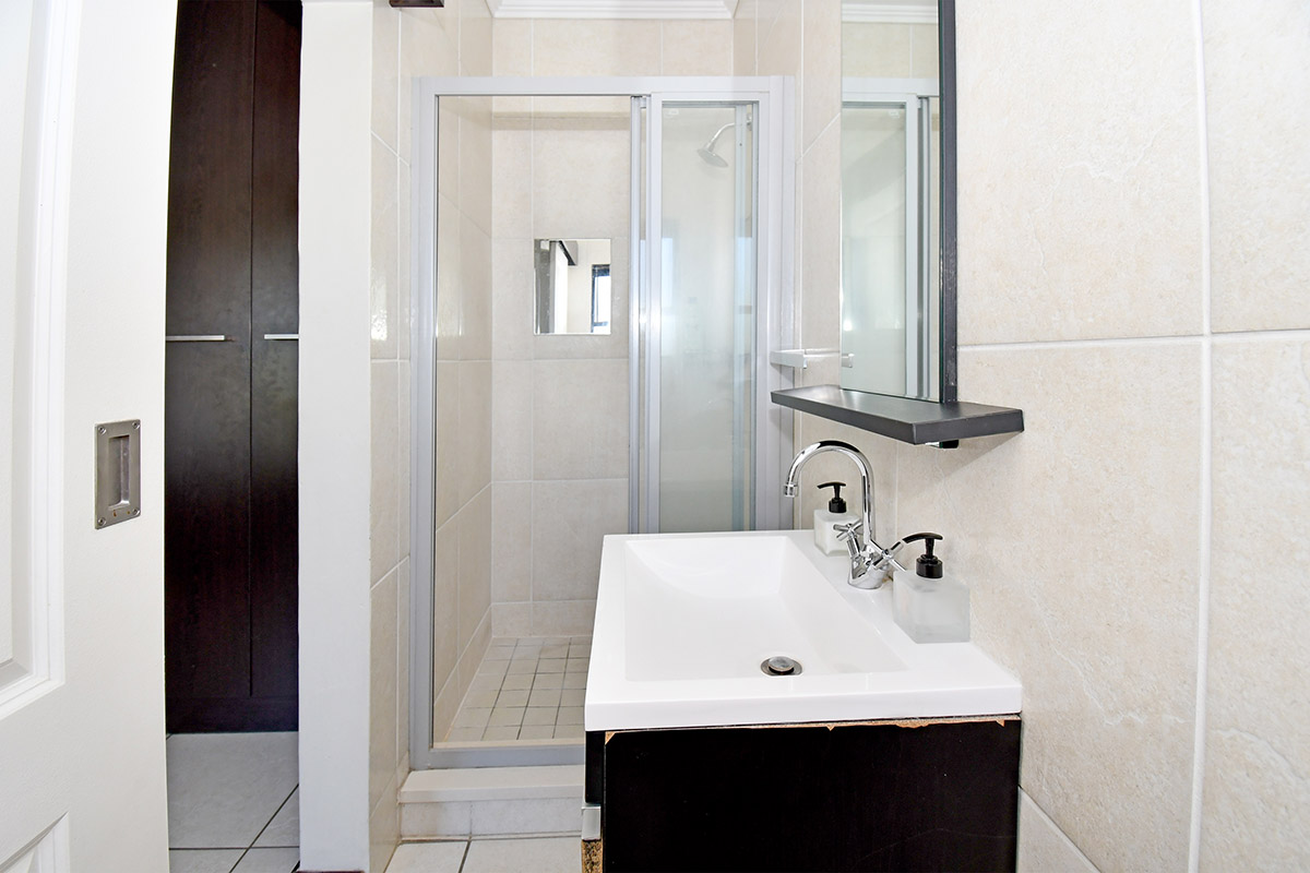 A compact bathroom featuring a tiled shower enclosure, a modern vanity basin with mixer tap, and built-in storage cabinetry.