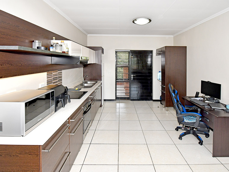 A functional kitchen featuring dark wood cabinetry, white countertops, integrated appliances, and tiled flooring, with direct access to an exterior security door.