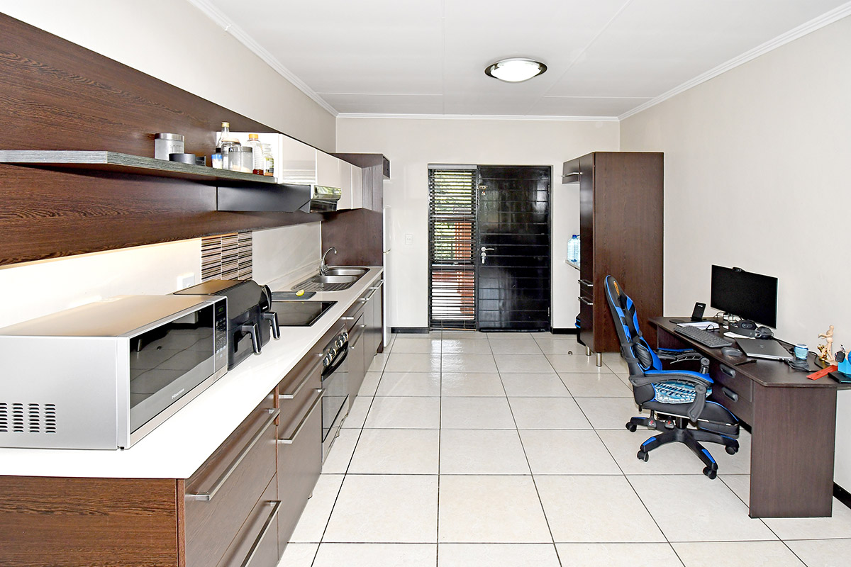 A functional kitchen featuring dark wood cabinetry, white countertops, integrated appliances, and tiled flooring, with direct access to an exterior security door.