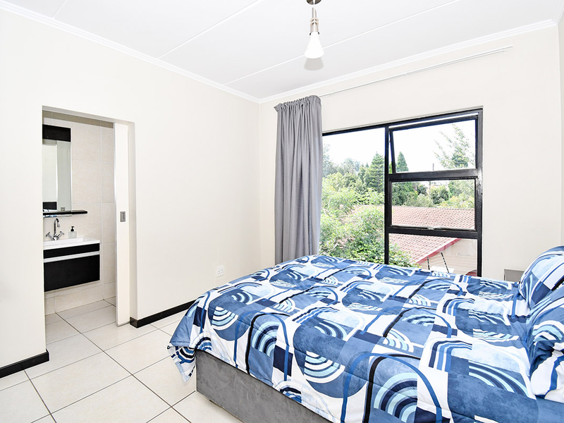 A well-lit bedroom featuring tiled flooring, an en-suite bathroom with a modern vanity, and large windows offering a pleasant outdoor view.