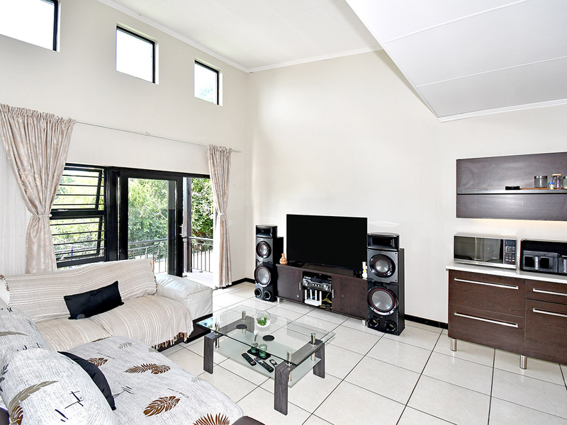 Spacious open-plan living area featuring high vaulted ceilings, tiled floors, and large sliding doors leading to an outdoor balcony.