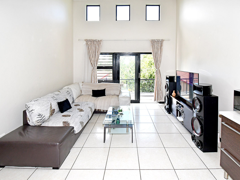 Spacious open-plan living area featuring high ceilings, clerestory windows, tiled flooring, and direct access to a balcony through sliding glass doors.