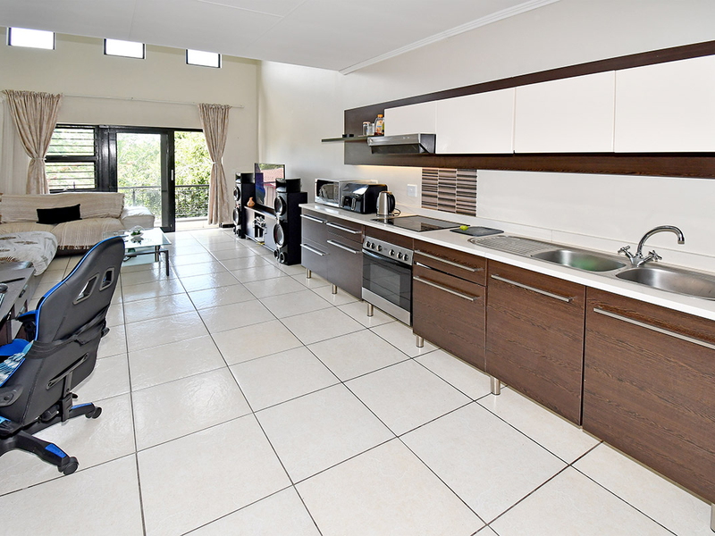 Open-plan living area featuring a modern kitchen with dark wood cabinetry, stainless steel appliances, tiled flooring, and access to a balcony through sliding doors.