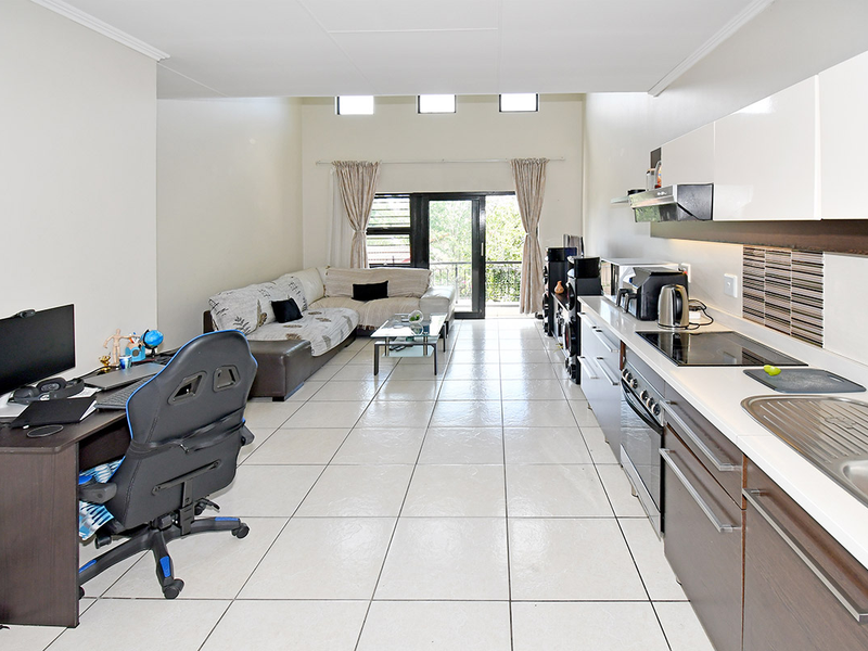 Open-plan living area featuring a modern kitchen with built-in cabinetry, electric hob, and tiled flooring, leading to a balcony through sliding glass doors.