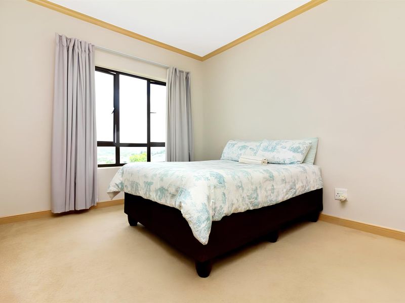 A well-lit bedroom featuring neutral carpeting, beige walls with crown molding, and a large window providing natural light.