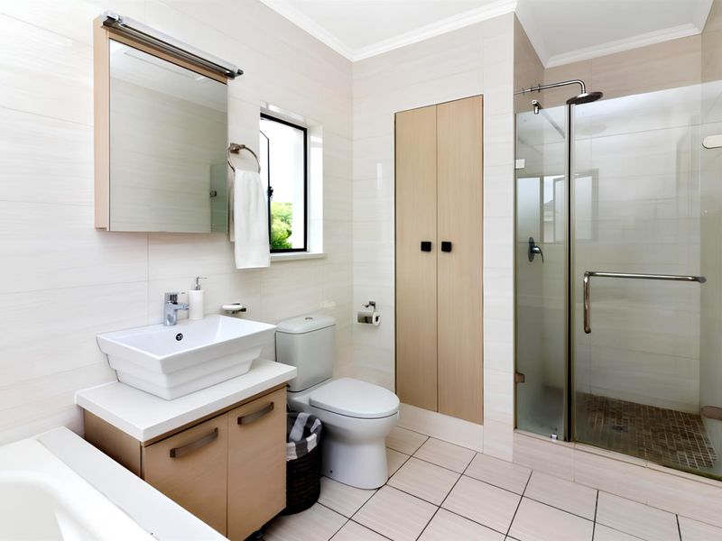 Modern bathroom featuring a vessel sink vanity, glass-enclosed shower, built-in storage cabinetry, and neutral wall and floor tiling.